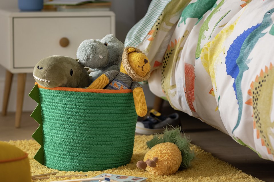 A dino rope basket in green and orange with stuffed toys in it.